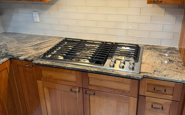 Gas cooktop installed in a granite countertop under a range hood