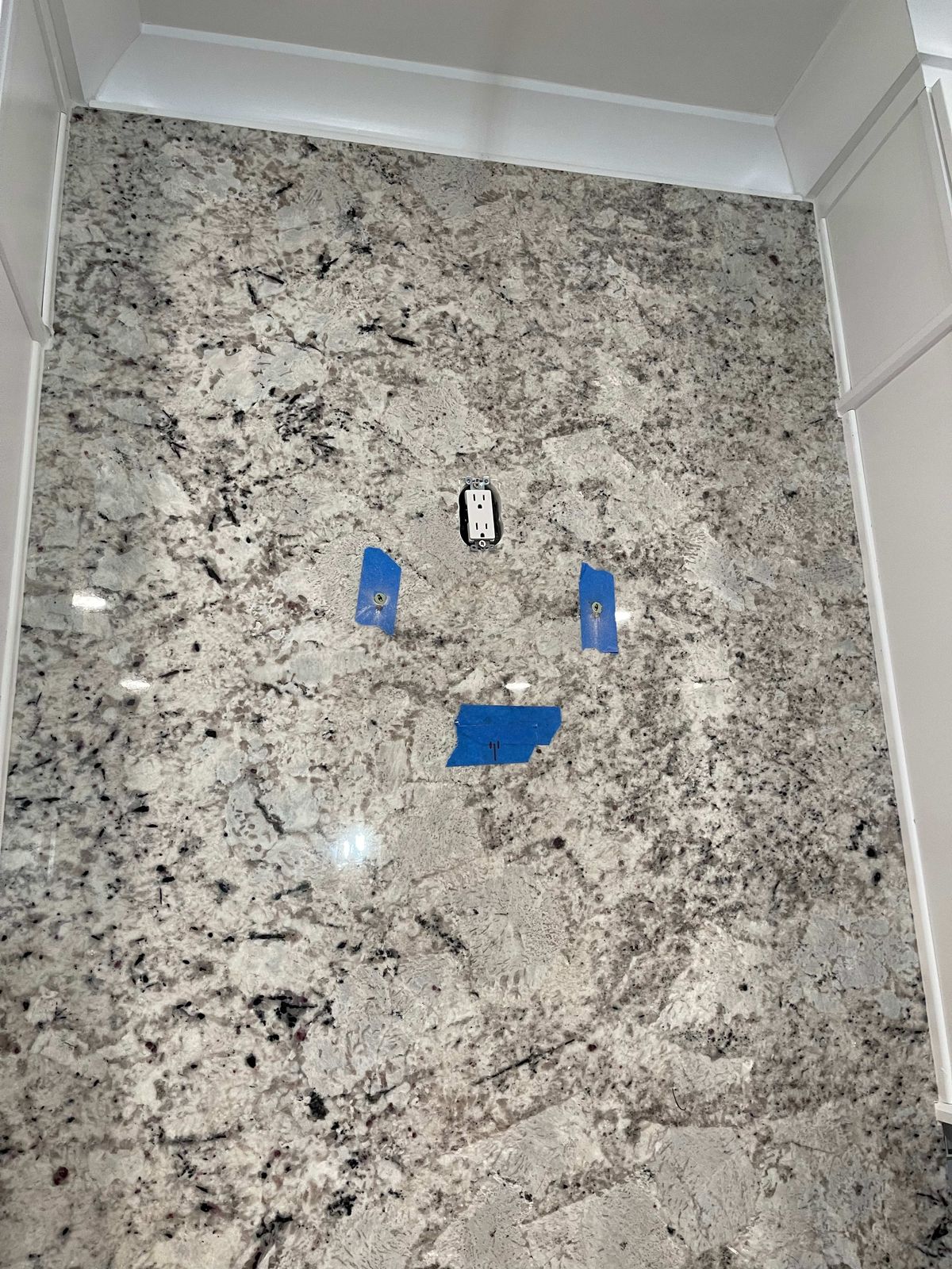 La misma pared de granito antes de instalar, con los anclajes marcados con cinta azul